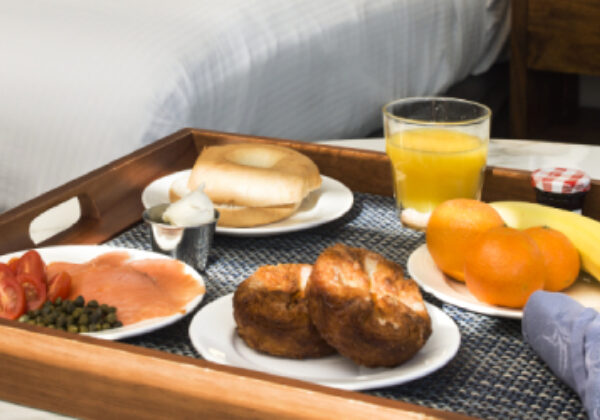 Continental breakfast tray next to the bed with bagel, cream cheese, lox, capers, tomatoes, muffins, fresh fruit, coffee and juice.