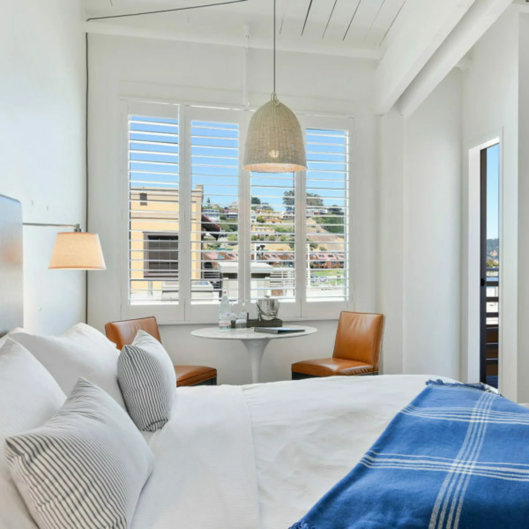 Bright, light, and contemporary guestroom with plush king bed and throw blanket, table for two, outdoor access with water view